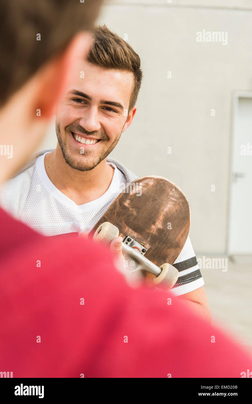 Junger Mann mit Skateboard lächelnd an Freund im freien Stockfoto