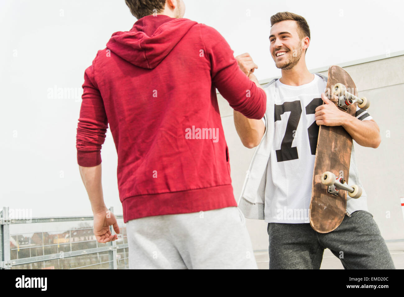 Junger Mann mit Skateboard Händeschütteln mit Freund im freien Stockfoto