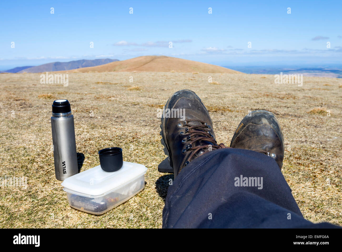 Walker mit Füße hoch und ein Lunchpaket auf Stybarrow Dodd mit den abgerundeten Gipfel von Watsons Dodd im Hintergrund Lake District Stockfoto