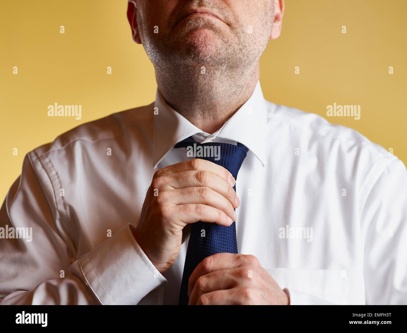 Großaufnahme, männlich in weißem Hemd und blaue Krawatte, er anziehen Krawatte Knoten, gelber Hintergrund Stockfoto