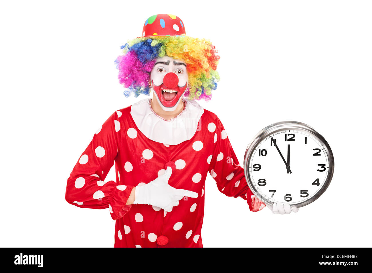 Junge männliche Clown eine große Wanduhr in einer Hand halten und in Richtung der Uhr mit den anderen isoliert auf weißem Hintergrund Stockfoto