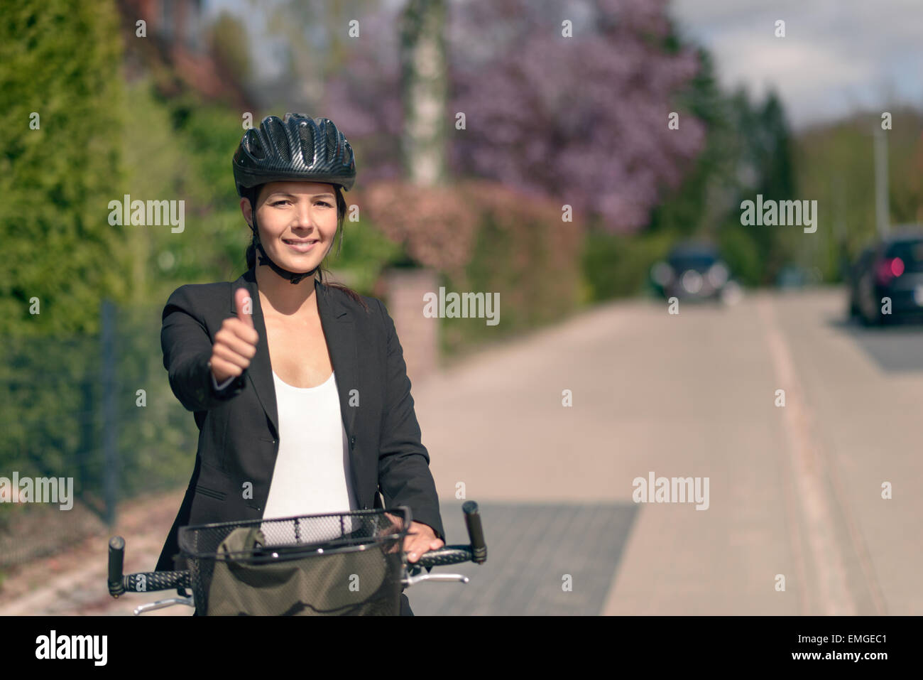 Aktive Geschäftsfrau auf ihrem Fahrrad mit Helm zeigt Daumen nach oben und schaut in die Kamera Lächeln. Stockfoto