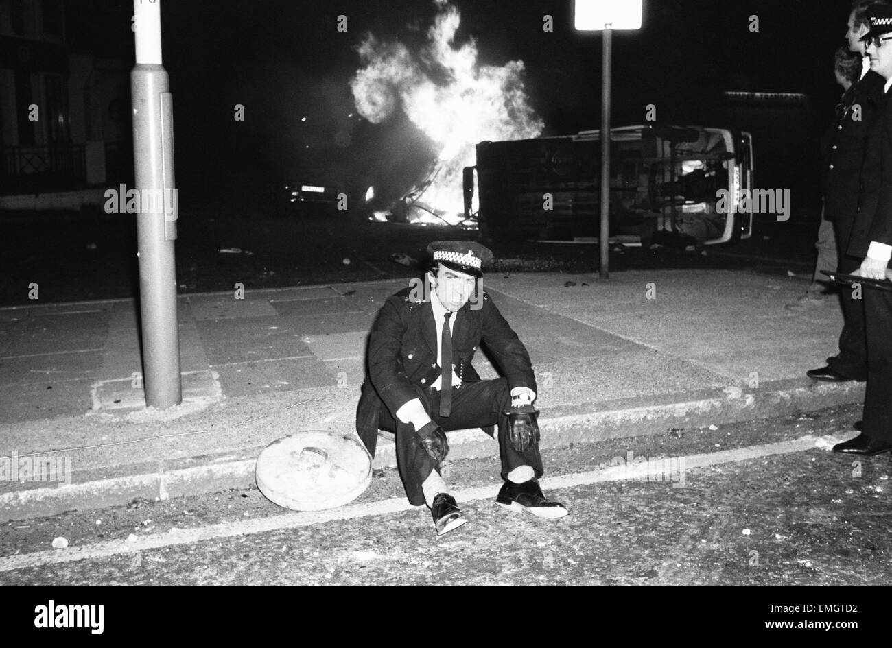 Eine erschöpfte Polizist ruht auf dem Bordstein, wie ein Feuer hell hinter ihm brennt nach Rassenunruhen in Southall, Westlondon ausbrach. Die Probleme begannen bei Bussen von Skinheads Front National Parolen skandierten und verteilen von Flugblättern in der Gegend. Die 200 starken Mob begann dann Zerschlagung Schaufenstern und angreifende Bevölkerung provozieren einen Aufstand von etwa 1000 asiatische Jugendliche verlassen ihre Heimat zu wehren. 6. Juli 1981. Stockfoto