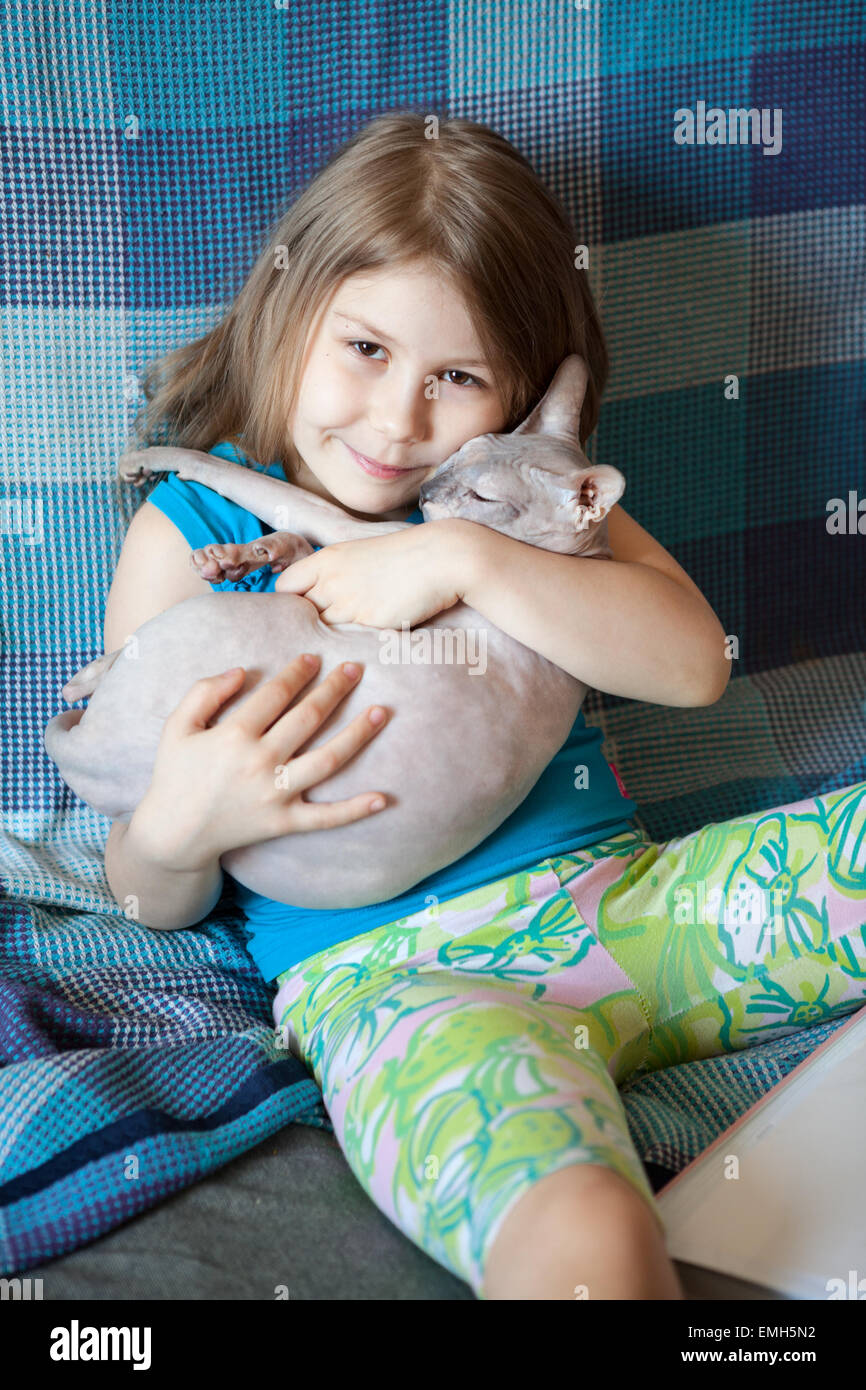 Glücklich, fröhlich Vorschulalter Mädchen umarmen Sphynx Katzen auf Couch zu Hause Stockfoto