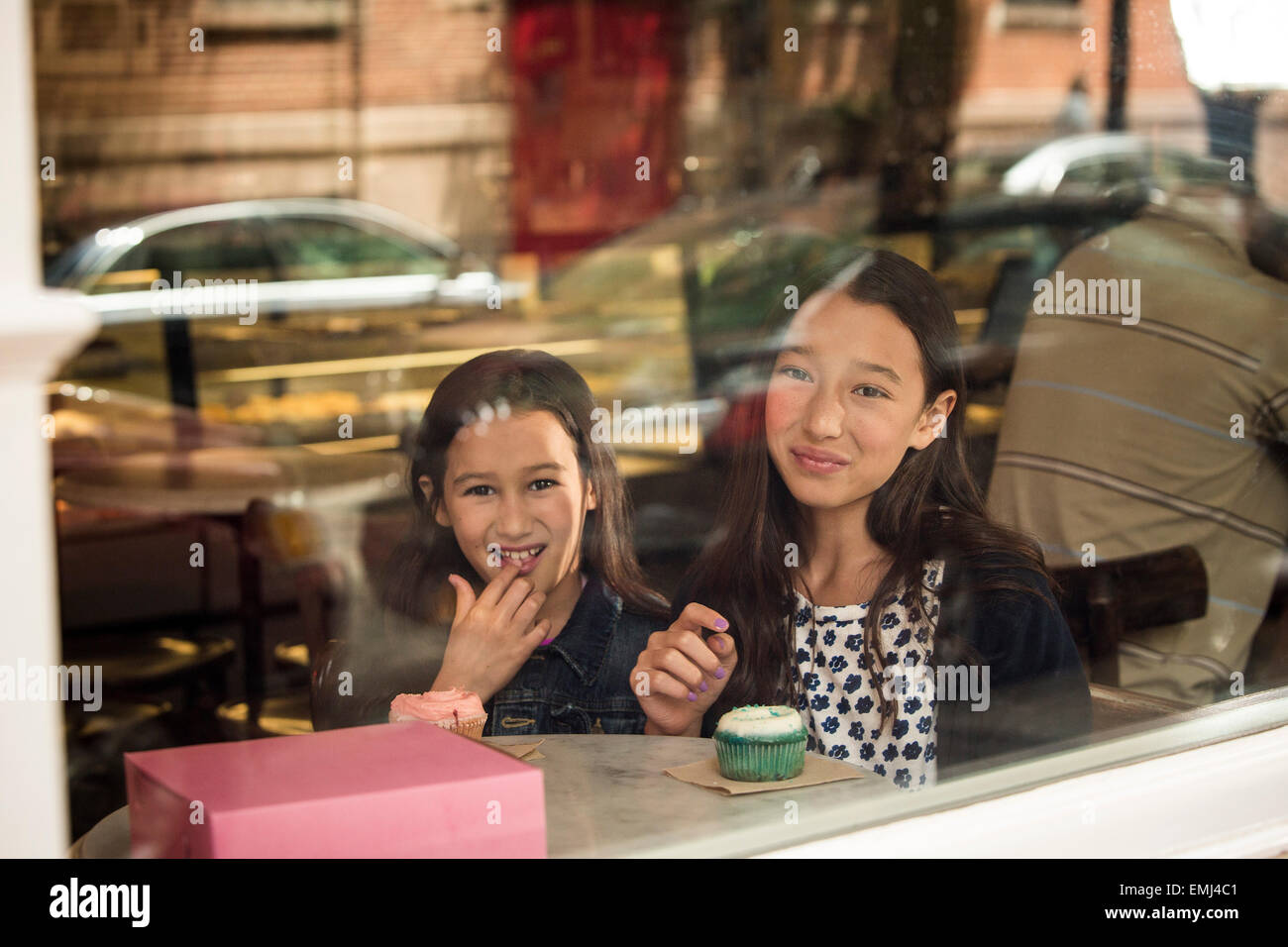 Zwei junge Mädchen essen Cupcakes im Café Fenster Stockfoto