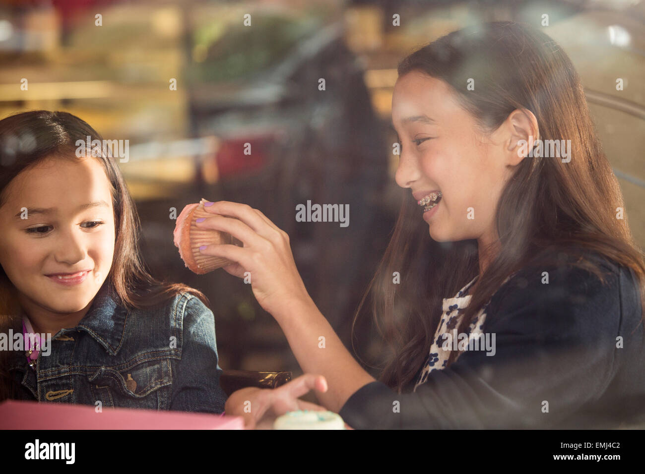 Zwei lächelnde junge Mädchen essen Cupcakes im Café Fenster Stockfoto