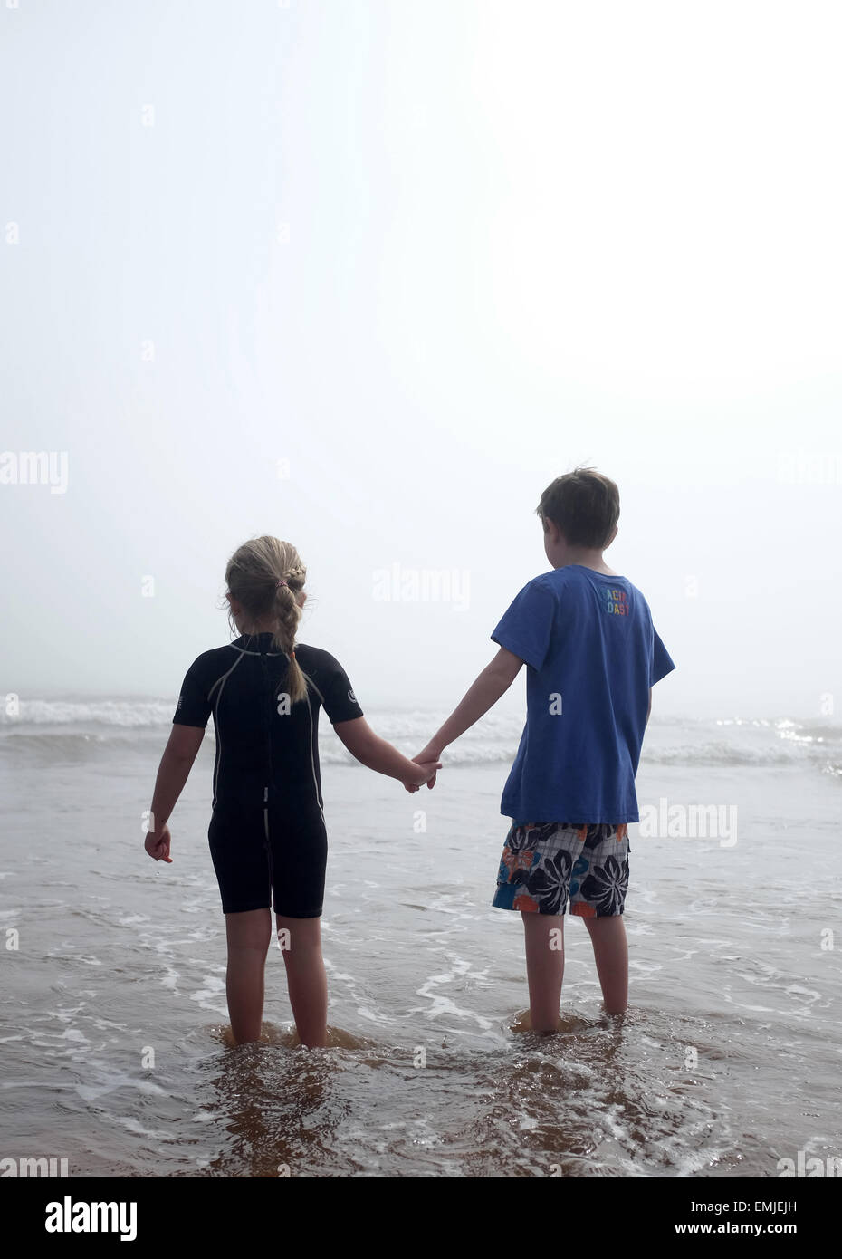 Ein kleiner Junge und ein Mädchen Hand in Hand Blick auf das Meer an einem nebligen Tag Stockfoto