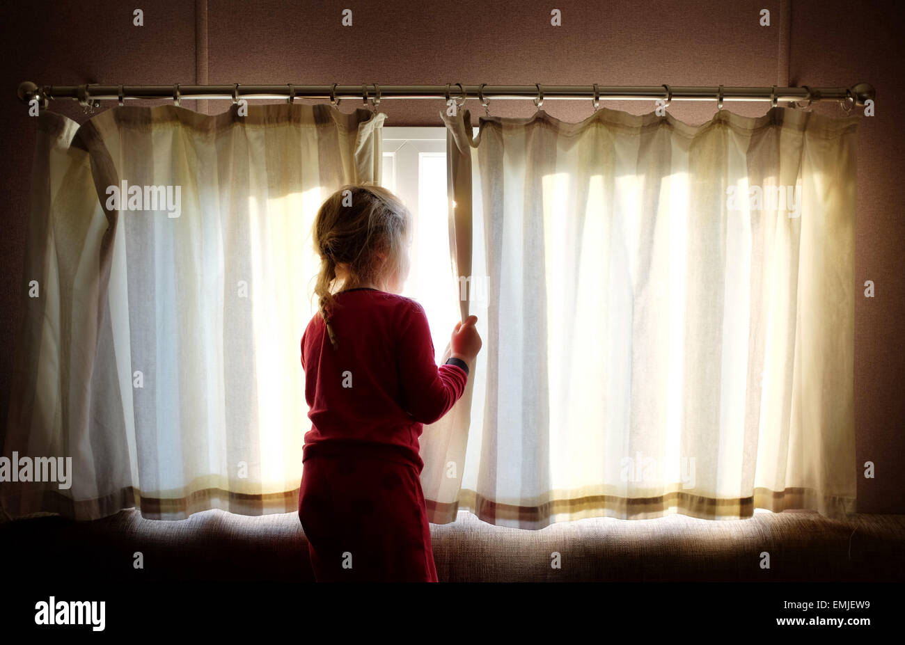 Ein verschlafenes junges Mädchen im Schlafanzug öffnet die Vorhänge, Blick aus dem Fenster zu Beginn eines neuen Tages Stockfoto