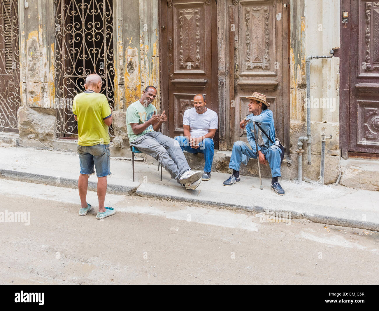 Vier kubanische Männer sitzen vor dem Eingang zu einem ihrer Häuser in Havanna Vieja und reden. Stockfoto