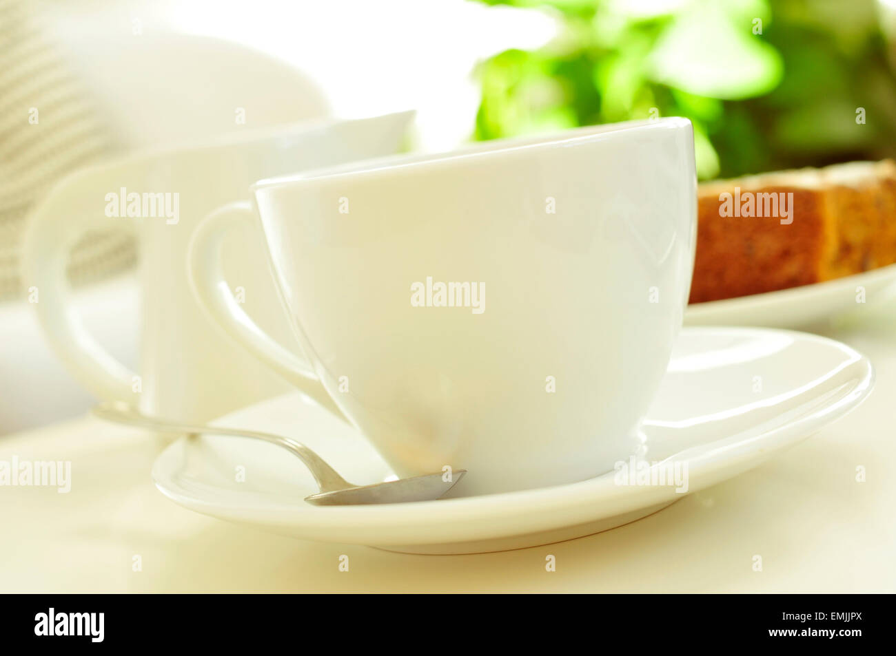 Nahaufnahme einer weißen Porzellan Tasse mit Kaffee oder Tee, und einen Milchtopf und ein Stück Kuchen im Hintergrund auf einem Couchtisch Stockfoto