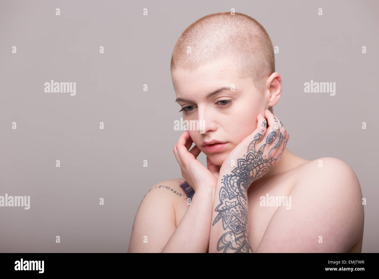 Eine junge Frau mit einem rasierten Kopf und Tattoos auf die Schulter, Arme und Hände Stockfoto