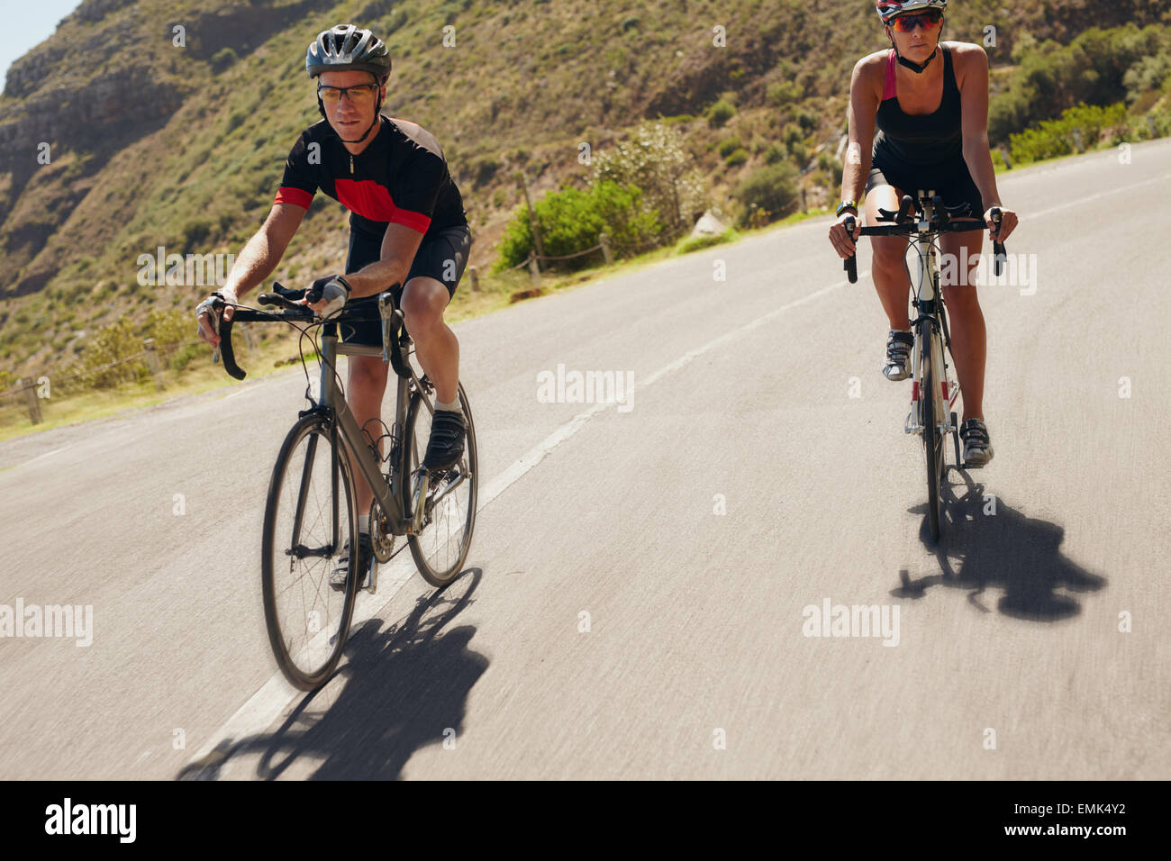 Zwei Athleten bergab auf Rennrädern. Mann und Frau Radfahrer fahren auf der Landstraße. Triathlon-Training. Stockfoto