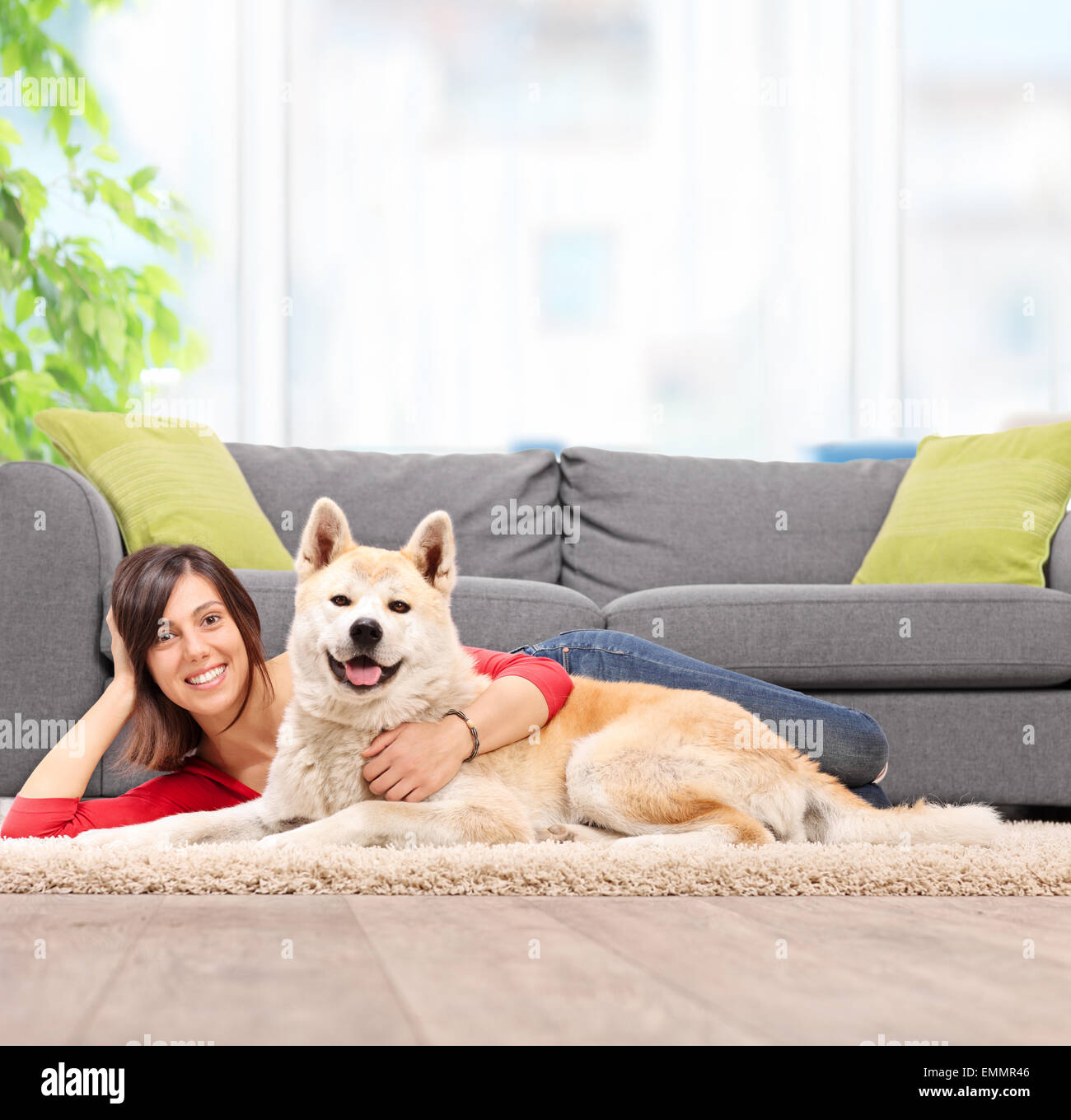 Junges Mädchen mit ihrem Hund auf dem Boden liegend und umarmen den Hund durch eine graue Couch zu Hause gedreht mit Tilt-Shift-Objektiv Stockfoto