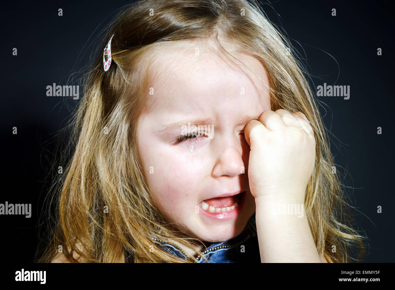 Niedliche kleine Mädchen mit Fokus auf ihre Tränen auf dunklem Hintergrund zu weinen Stockfoto