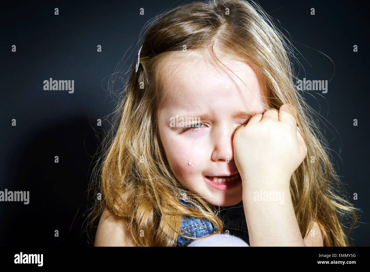 Niedliche kleine Mädchen mit Fokus auf ihre Tränen auf dunklem Hintergrund zu weinen Stockfoto