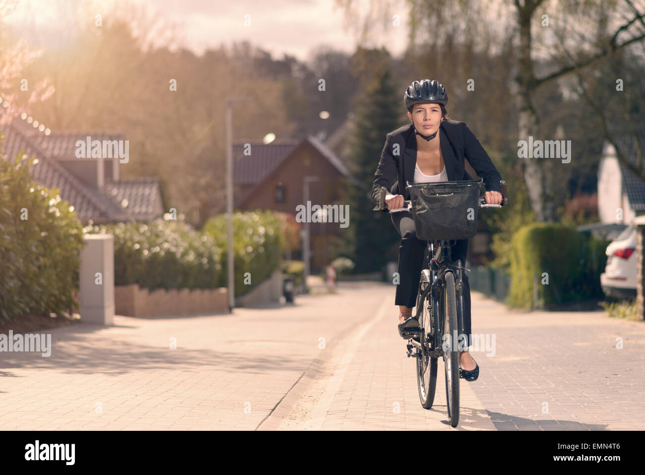 Junge Geschäftsfrau, die Fahrt zur Arbeit mit dem Fahrrad entlang einer Wohnstraße in ihrem stilvollen schlaff Anzug und Sicherheit Helm in einer eco Stockfoto