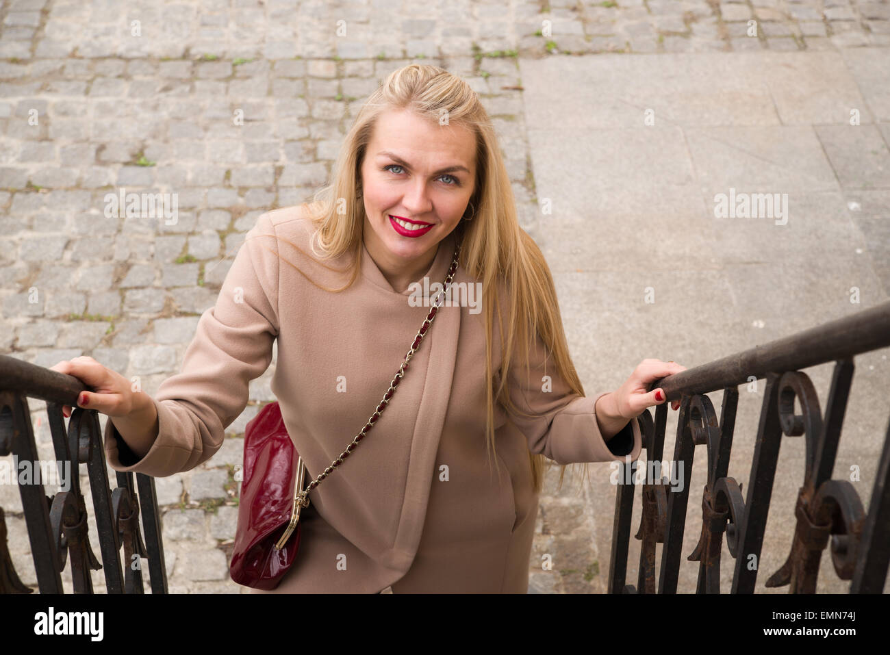 Junge Frau im Mantel lächelt und geht die Treppe hinauf Stockfoto