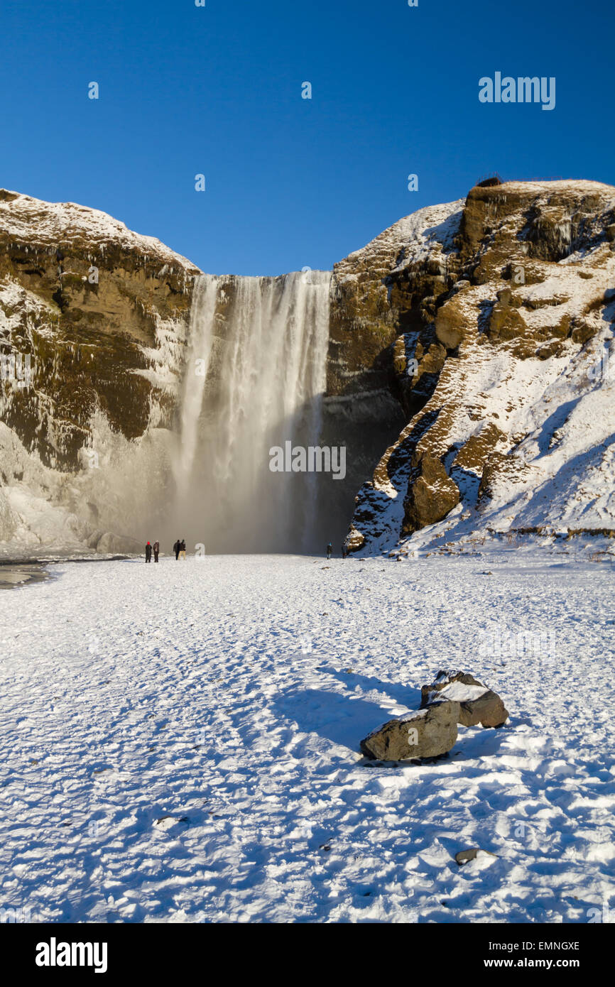 Touristen bewundern die Skogafoss Wasserfall in Island während der kurzen Wintertag Stockfoto