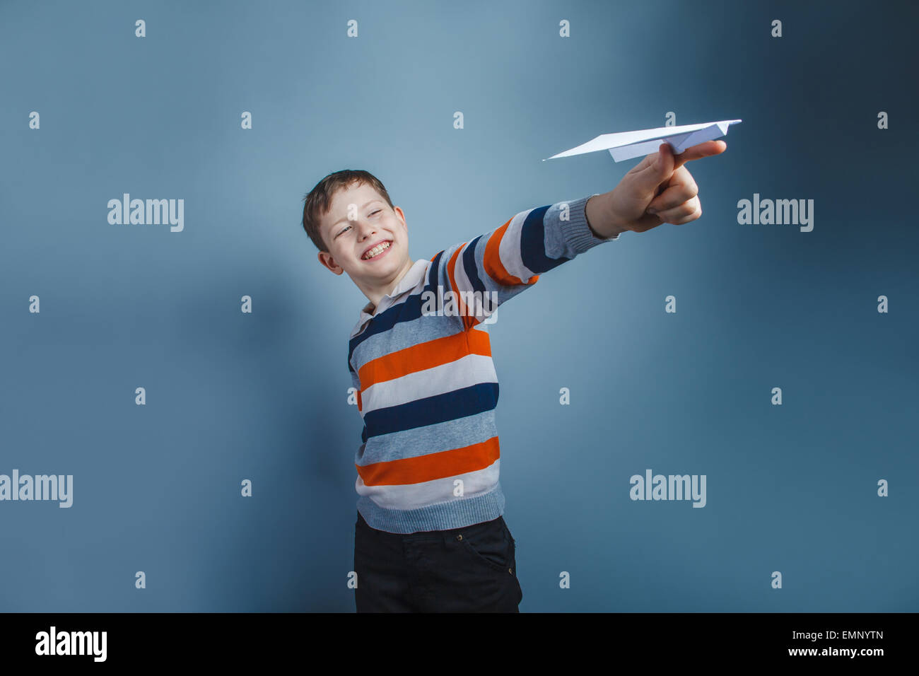 Europäisch anmutende junge von zehn Jahren spielen Papierflieger auf grauem Hintergrund Stockfoto