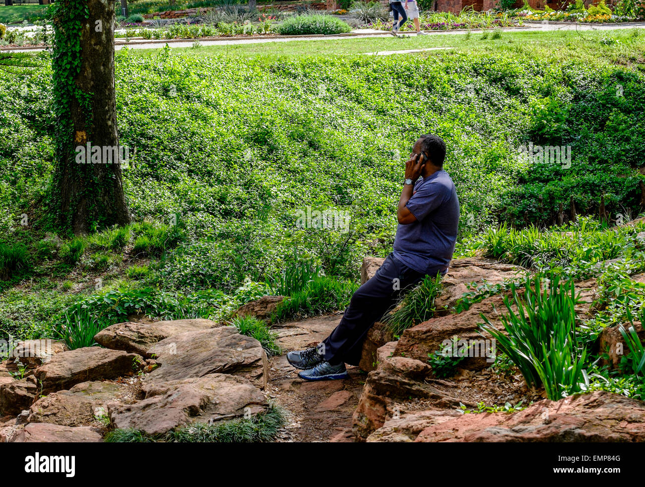 Ein afrikanischer amerikanischer Mann genießt einen öffentlichen Park während des Gesprächs auf seinem Handy. USA Stockfoto