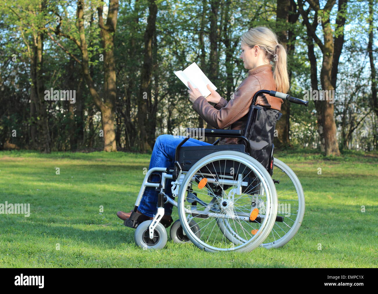 Eine Frau im Rollstuhl, die ein Buch in einem park Stockfoto
