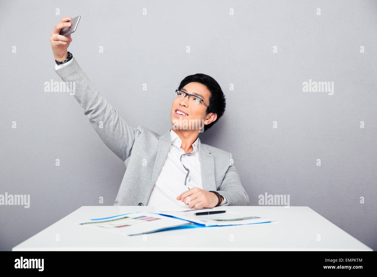 Glücklich Kaufmann am Tisch sitzen und Selfie Foto auf Smartphone über grauen Hintergrund Stockfoto