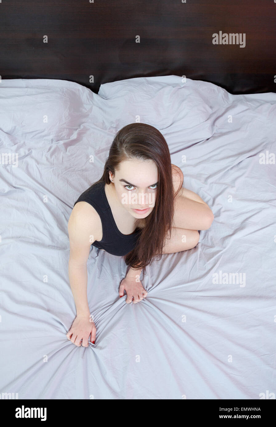 Porträt von sexy junge leidenschaftliche Frau oder Mädchen in verführerischen Pose auf grauen Blatt Bett im Schlafzimmer liegen und Blick auf Kamera oder y Stockfoto