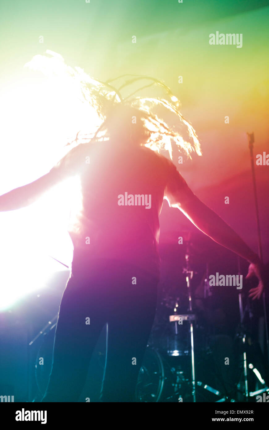 Flache Silhouette eines Musikers, der während eines Live-Rock-Konzerts auf einer pulsierenden Bühne Headbanging, mit Linsenflecken und Schlagzeug-Hintergrund. Stockfoto