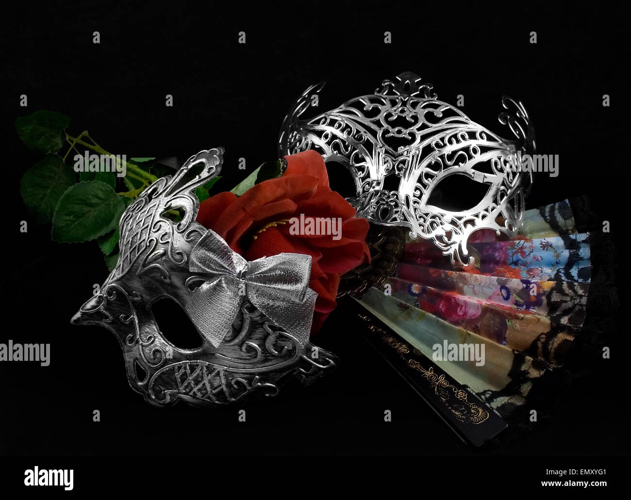 Masken mit Rose. Silber Karnevalsmasken mit klappbarer Ventilator und rote Rose auf schwarzem Stoff Hintergrund legen. Stockfoto