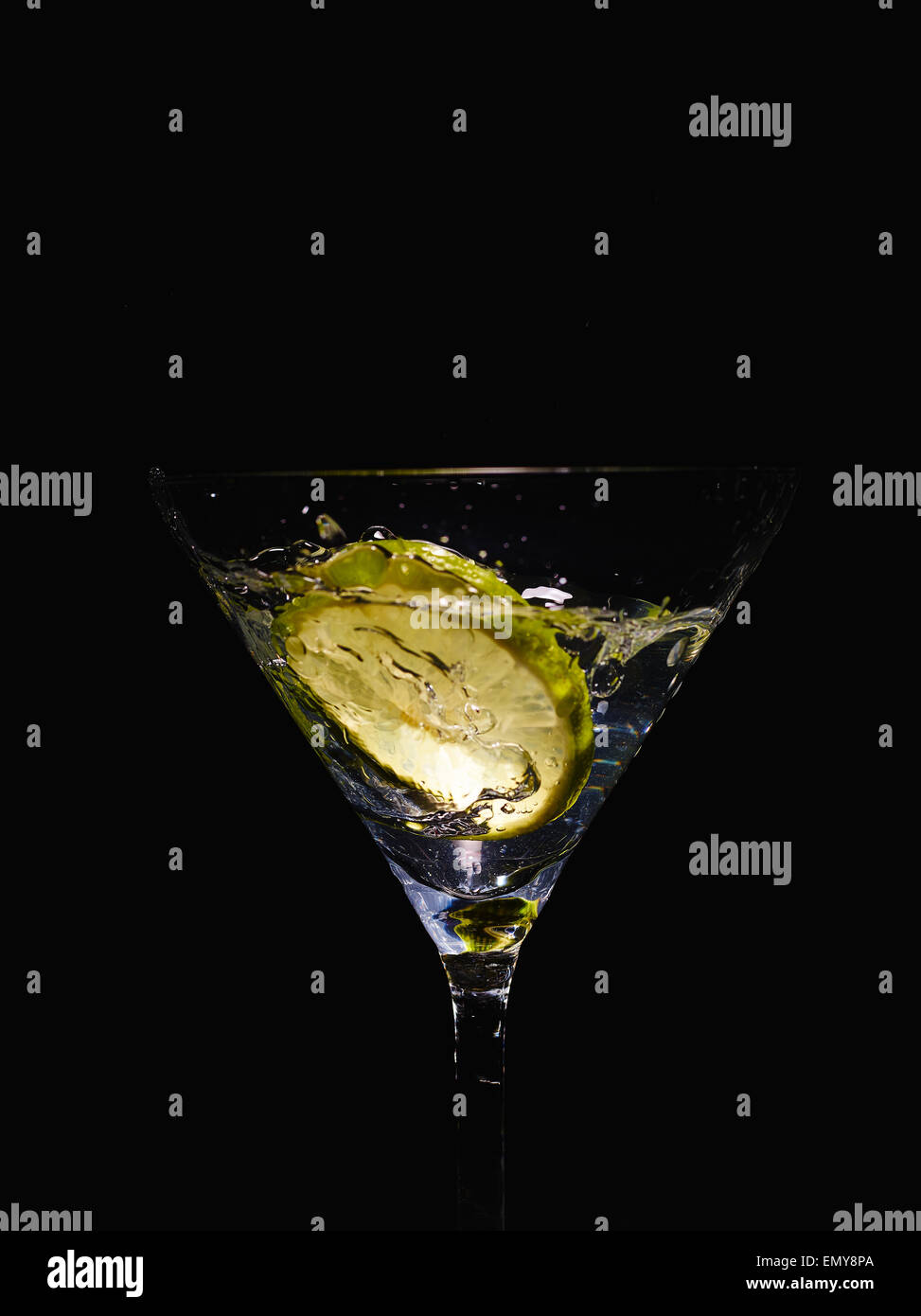 Martini-Glas und alkoholisches Getränk mit einer Limettenscheibe, Spritzer, schwarzer Hintergrund Stockfoto