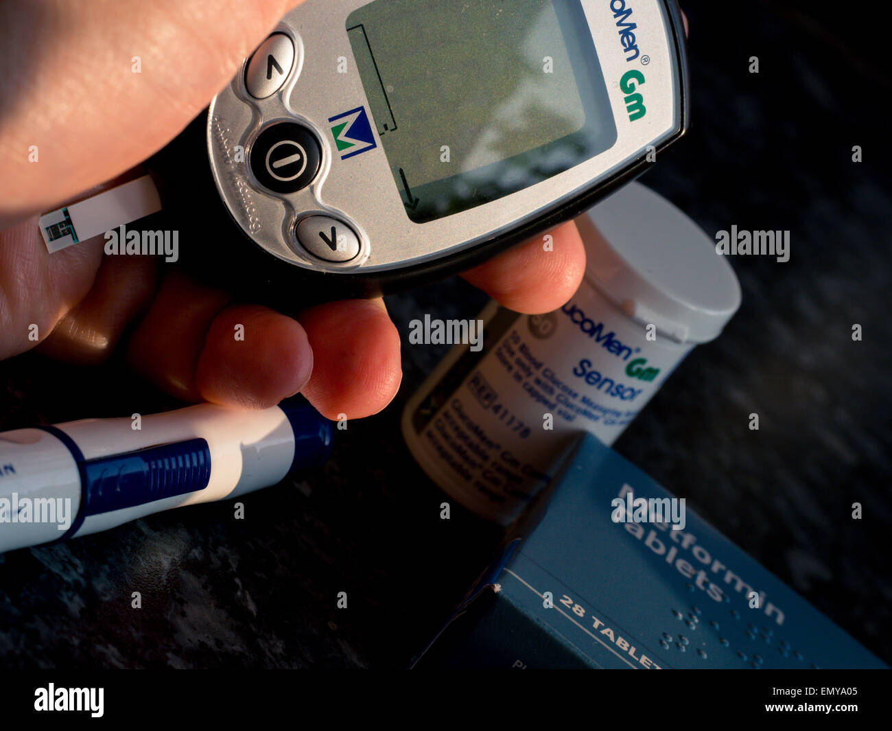 Eine Hand hält einen Diabetes Blut Glukose Leser mit anderen diabetischen Behandlungen im Hintergrund Stockfoto