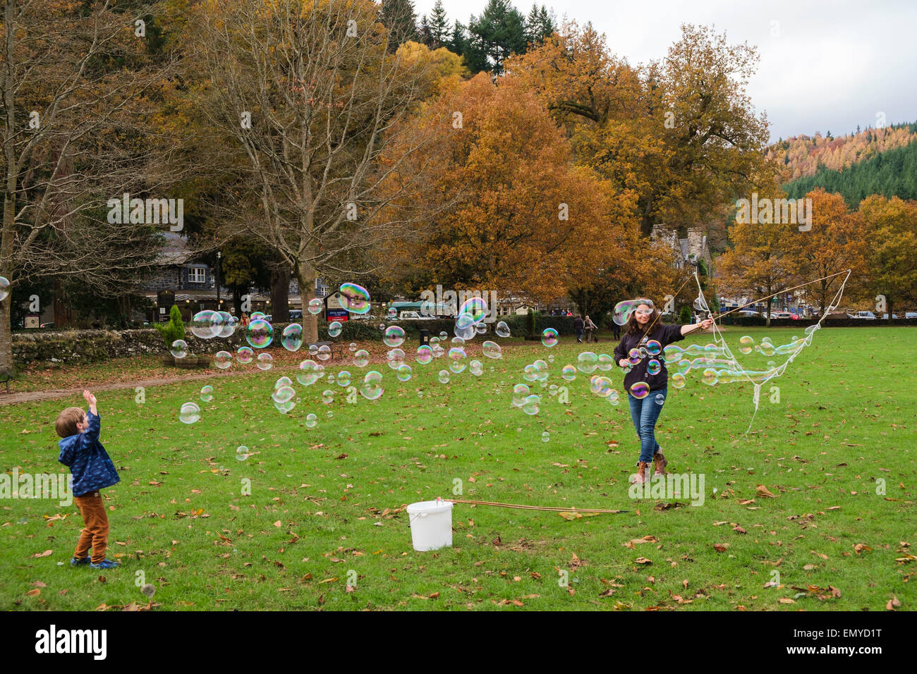 Ein kleiner Junge spielt mit vielen kleinen Seifenblasen gemacht durch eine Blase Stab auf Dorf in Betws-y-Coed Conwy North Wales UK grün Stockfoto