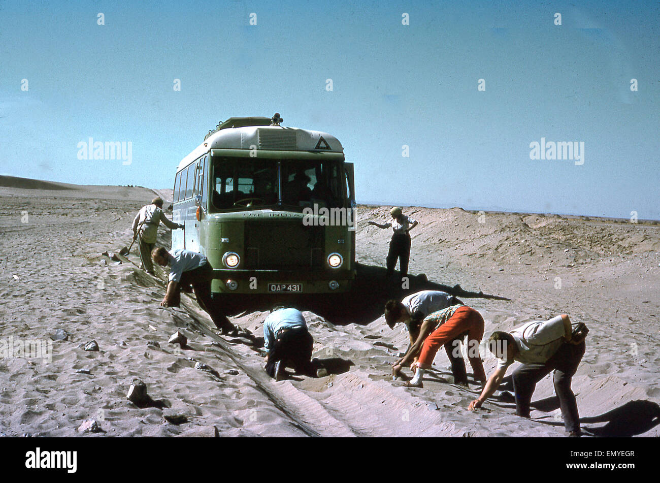 Etwa 1960, ein historisches Bild, das Passagiere vor dem transkontinentalen Bus, dem Indiamaner, zeigt, die die Route frei machen, die in der Thar Wüste oder der Great Indian Wüste im Sand feststeckt. Dieses Fernfahrzeug fuhr von London nach Bombay, Indien und dann zurück nach London. Stockfoto