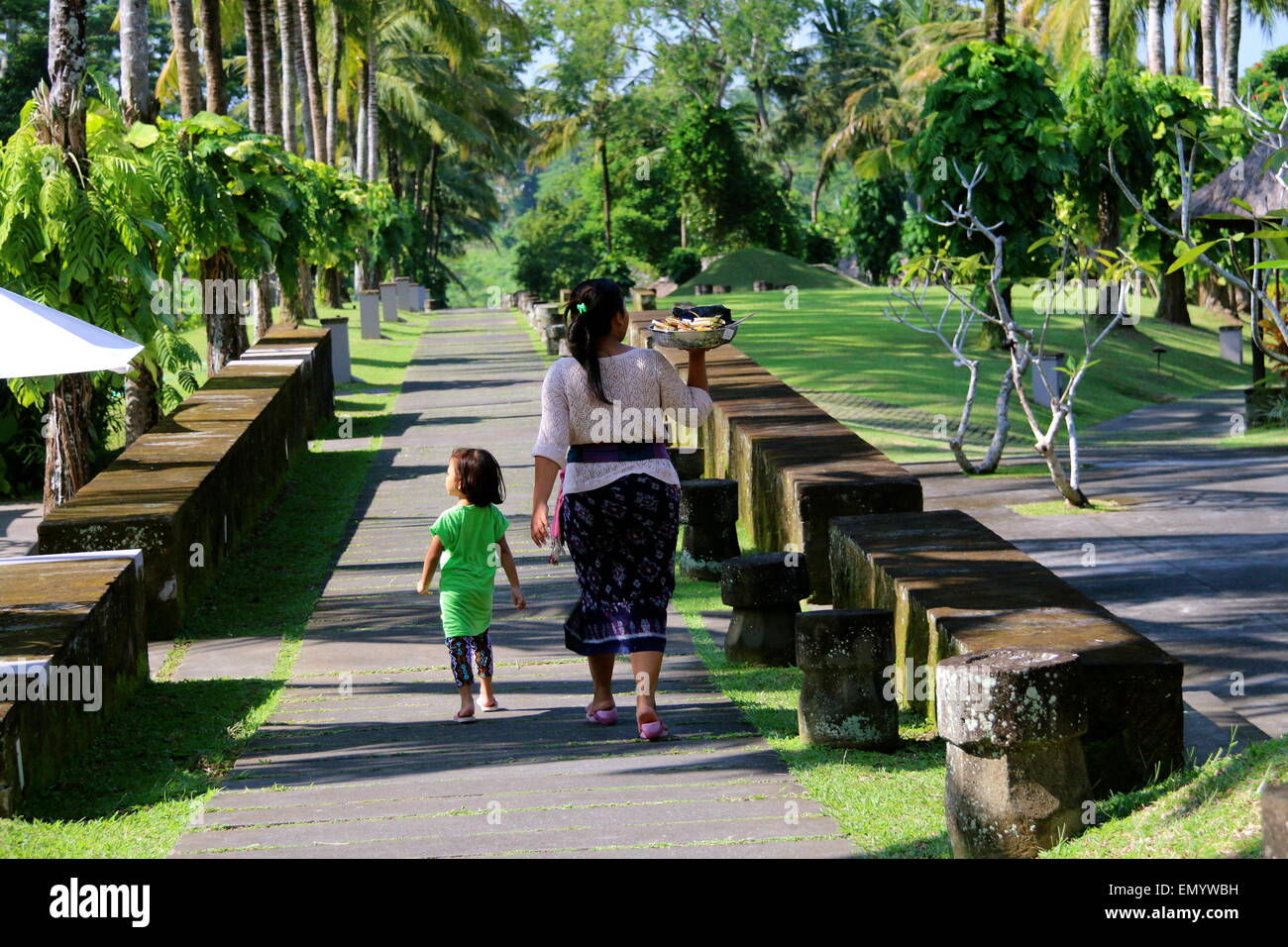 Eine balinesische Frau, begleitet von ihrer Tochter, deren Aufgabe tägliche heilige Angebot zu den Tempeln im Resort liefert. Stockfoto