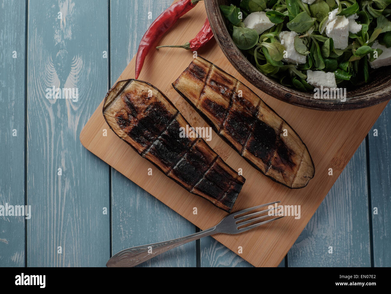 Hälften gebratene Auberginen und Salat auf einem Holztisch Stockfoto