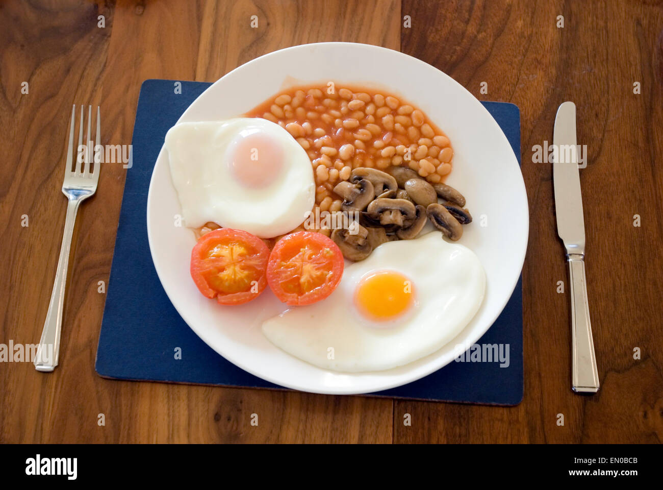 Komplettes englisches Frühstück für Vegetarier, Tomate, Ei, Pilz und Baked Beans, Gabel und Messer auf Holztisch Stockfoto