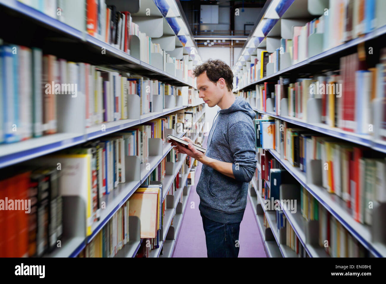 junger Student Buch zwischen den Regalen in der Bibliothek Stockfoto