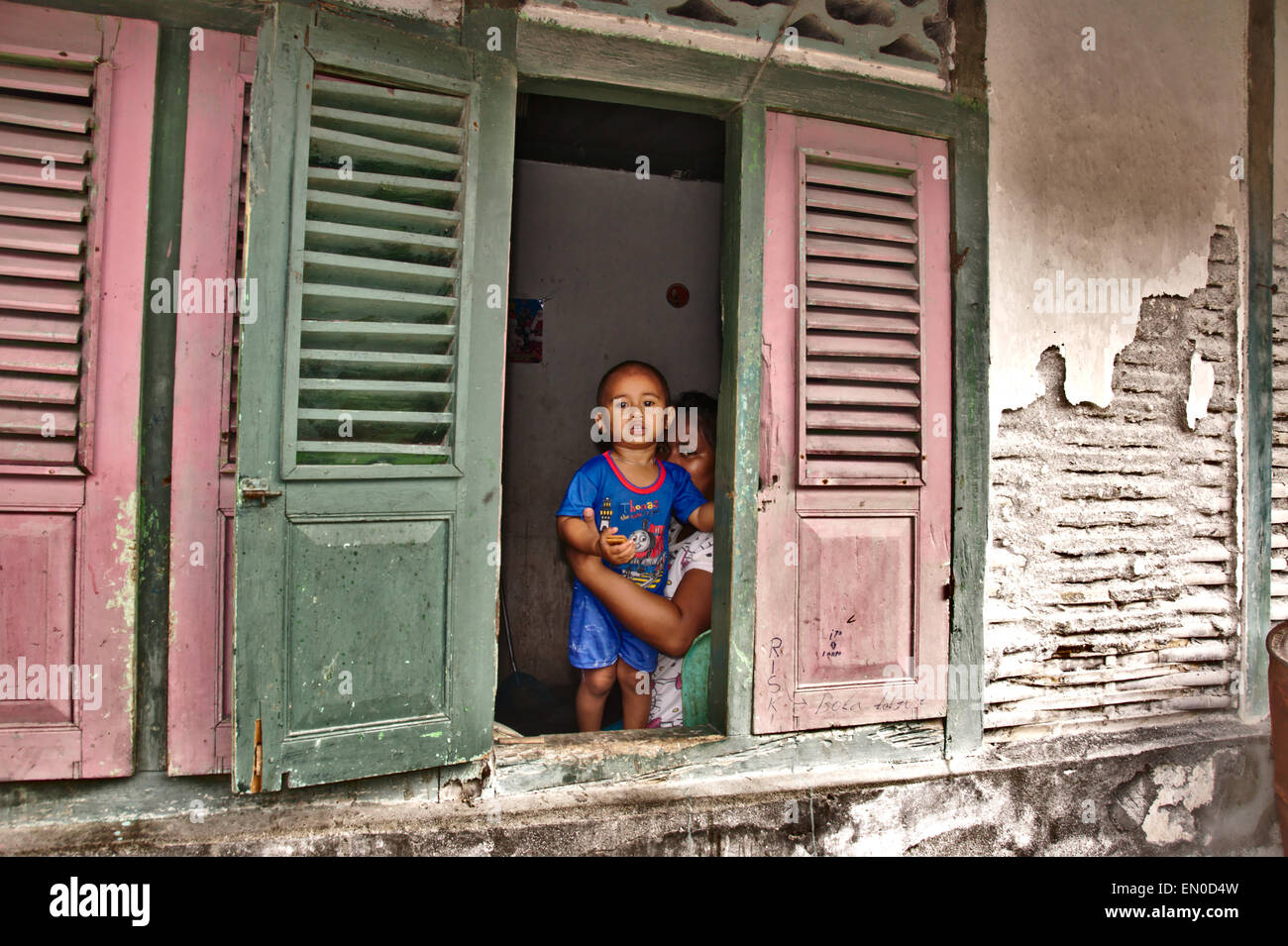 Ein kleiner Junge und seine Mutter schauen aus einem offenen Fenster ihres Hauses auf der Insel Tagulandang nördlich von Sulawesi in Indonesien. Stockfoto