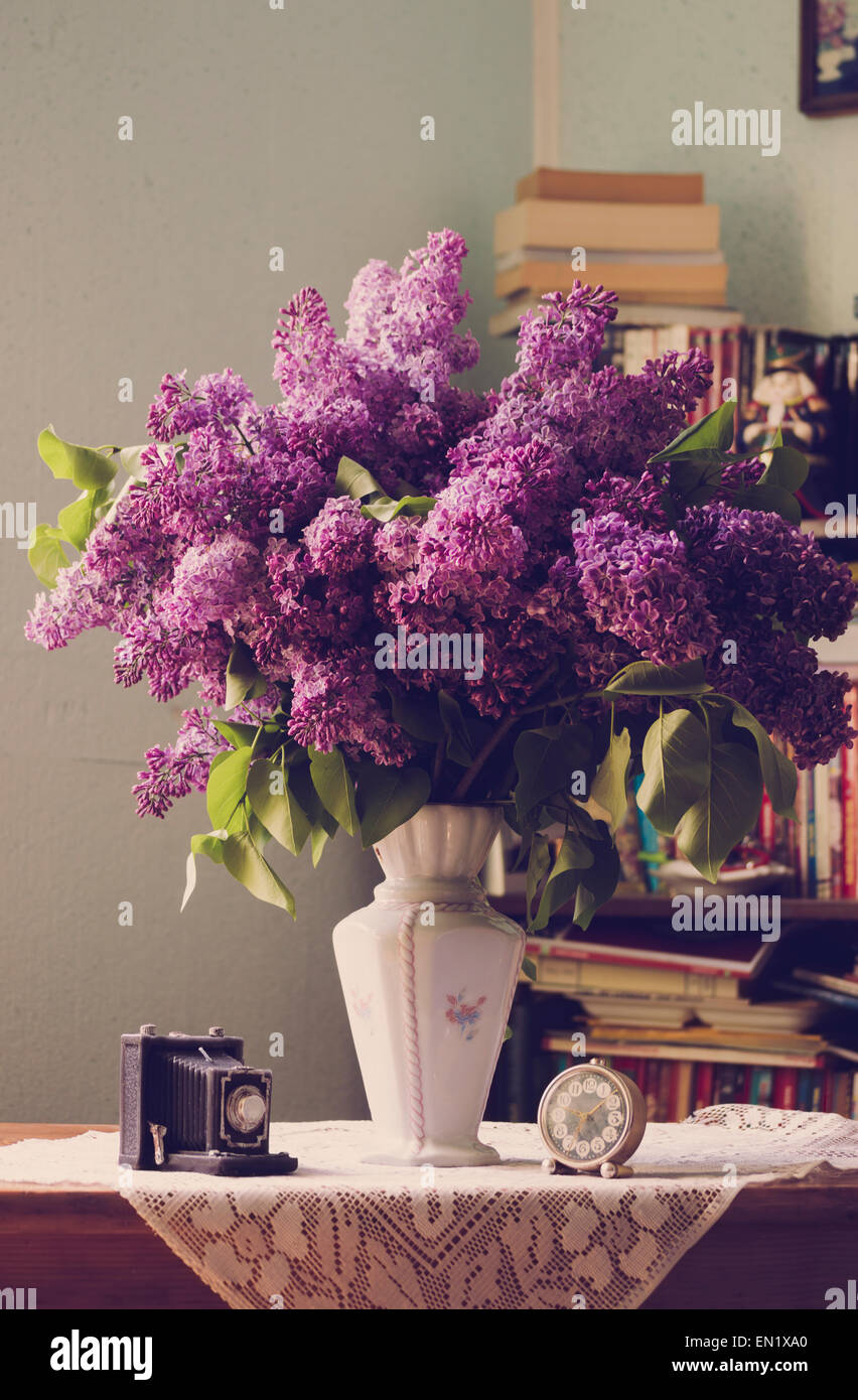 Flieder in der Vase und Zubehör in der Nähe der Bibliothek im Innenbereich mit natürlichem Licht. Stockfoto