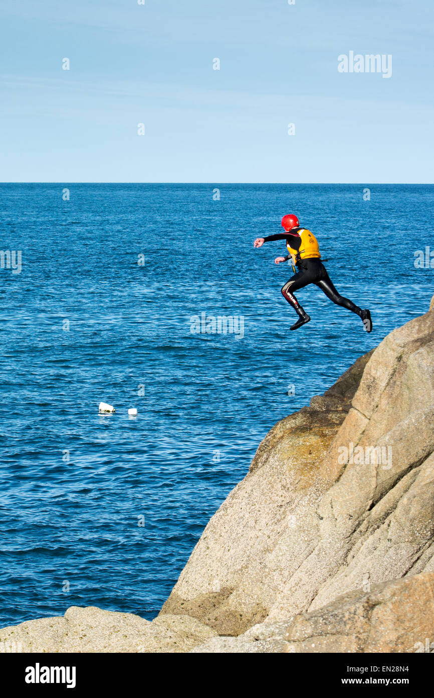 Mann im Anzug, Helm und Schwimmweste abspringen Felsen ins Meer eines der Coasteering Sportarten zu üben. Stockfoto