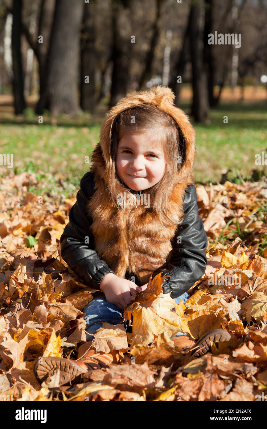 Mädchen in eine Pelzjacke sitzt auf das Herbstlaub gefallen-down Stockfoto
