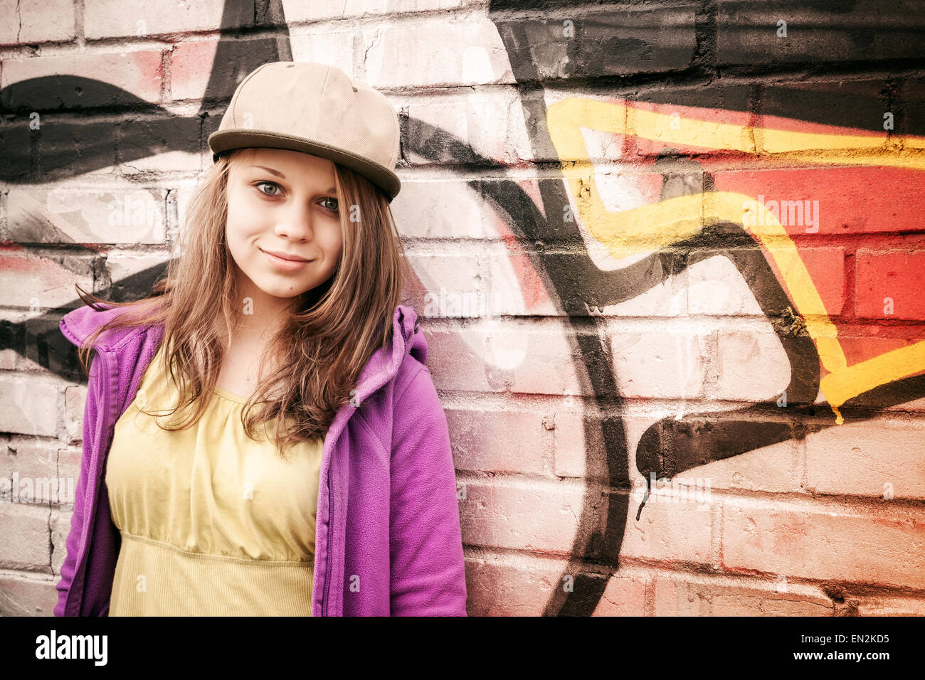 Stilvolle Teenager Blondine steht in der Nähe von städtischen Wand mit Graffiti, Foto mit warmen Retro-Tonwertkorrektur Wirkung, Instagram alte st Stockfoto