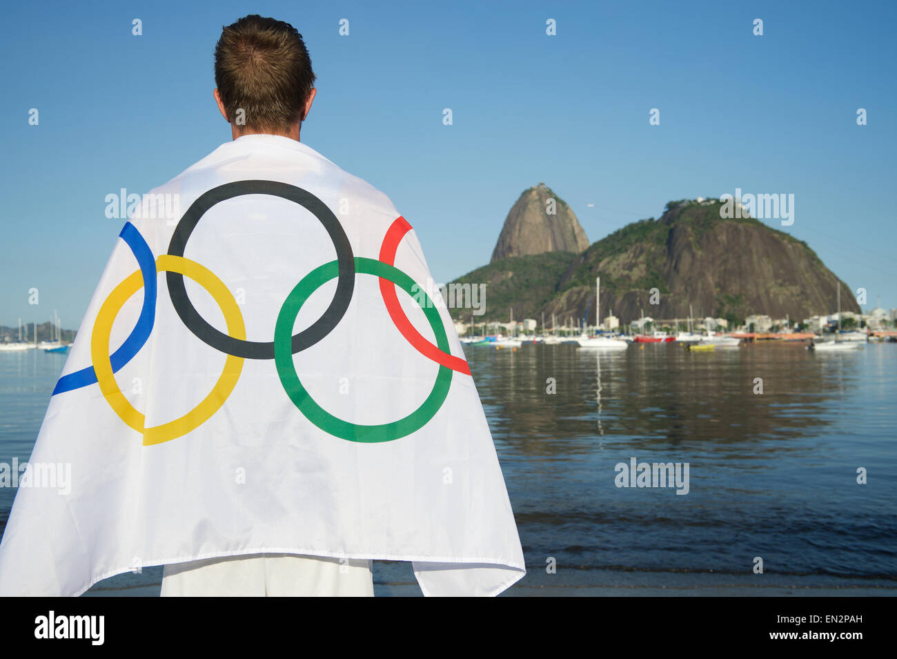 RIO DE JANEIRO, Brasilien - 24. März 2015: Mann im Olympischen Fahne drapiert steht an der Küste von Botafogo-Bucht vor Blick auf Suga Stockfoto