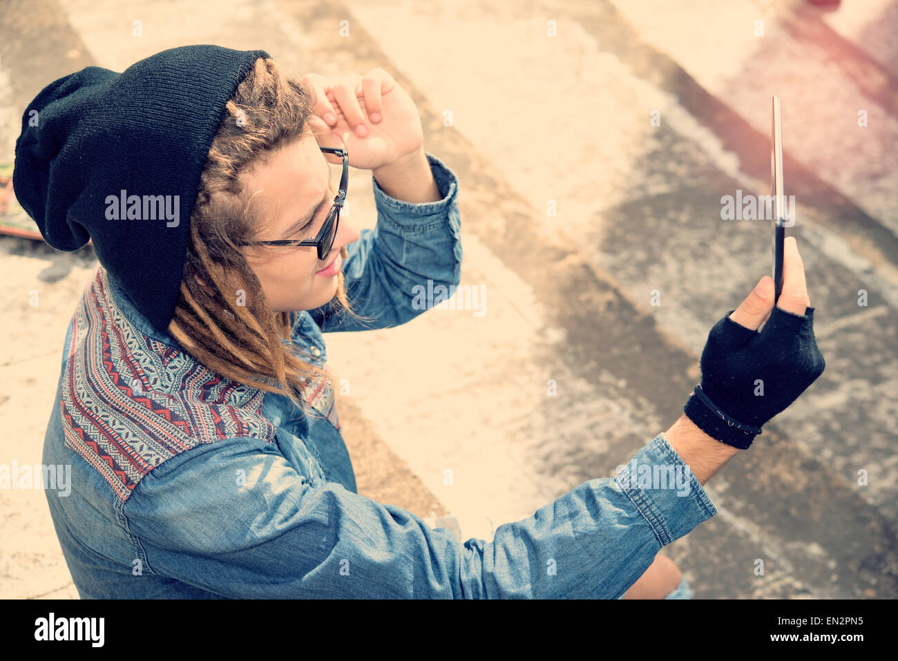 hübscher Kerl mit Dreadlocks sitzt auf der Treppe nehmen Selfie mit Tablet warm Filter angewendet Stockfoto