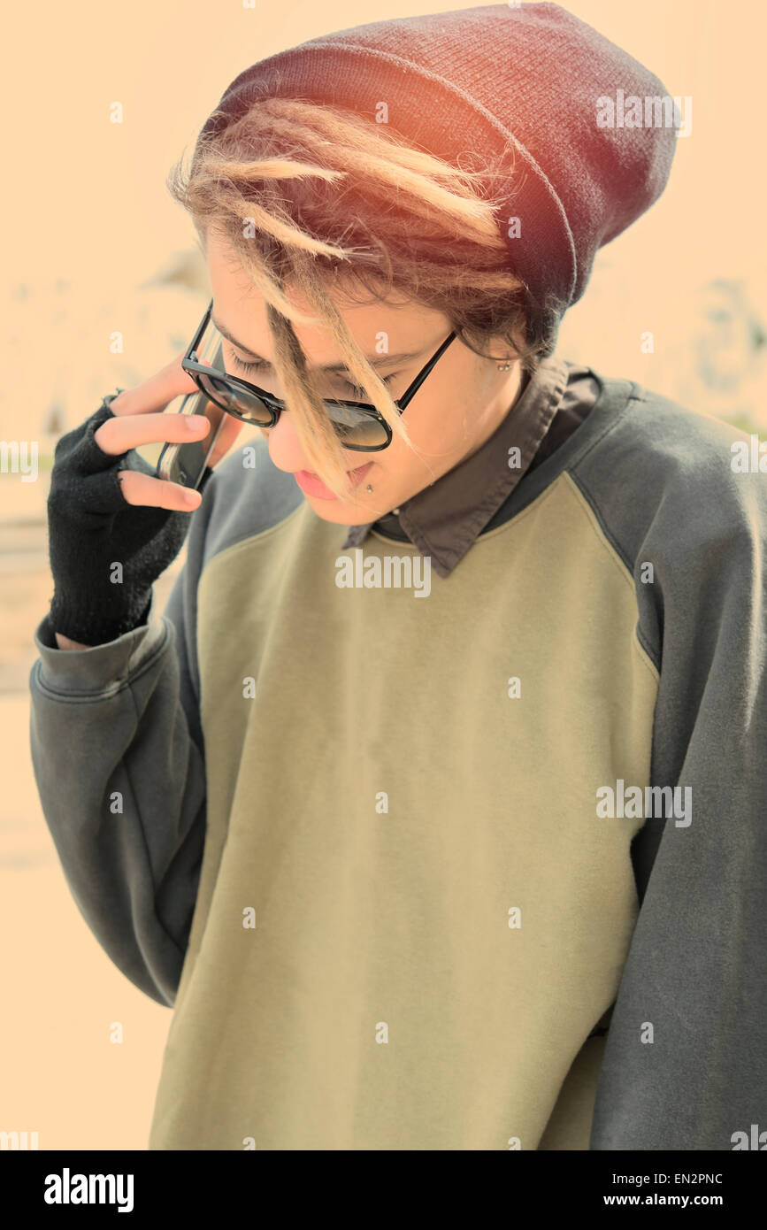 junger Kerl im Freien mit Rasta Haar mit Smartphone in ein Lifestyle-Konzept mit einem warmen Filter angewendet selektiven Fokus auf Gläsern Stockfoto