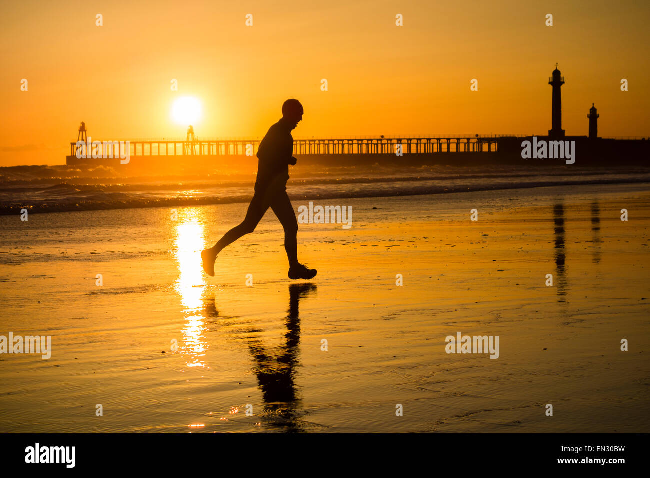Männliche Jogger Whitby mit am Strand die Sonne über die Piers in Bachground. Whitby, North Yorkshire, UK Stockfoto