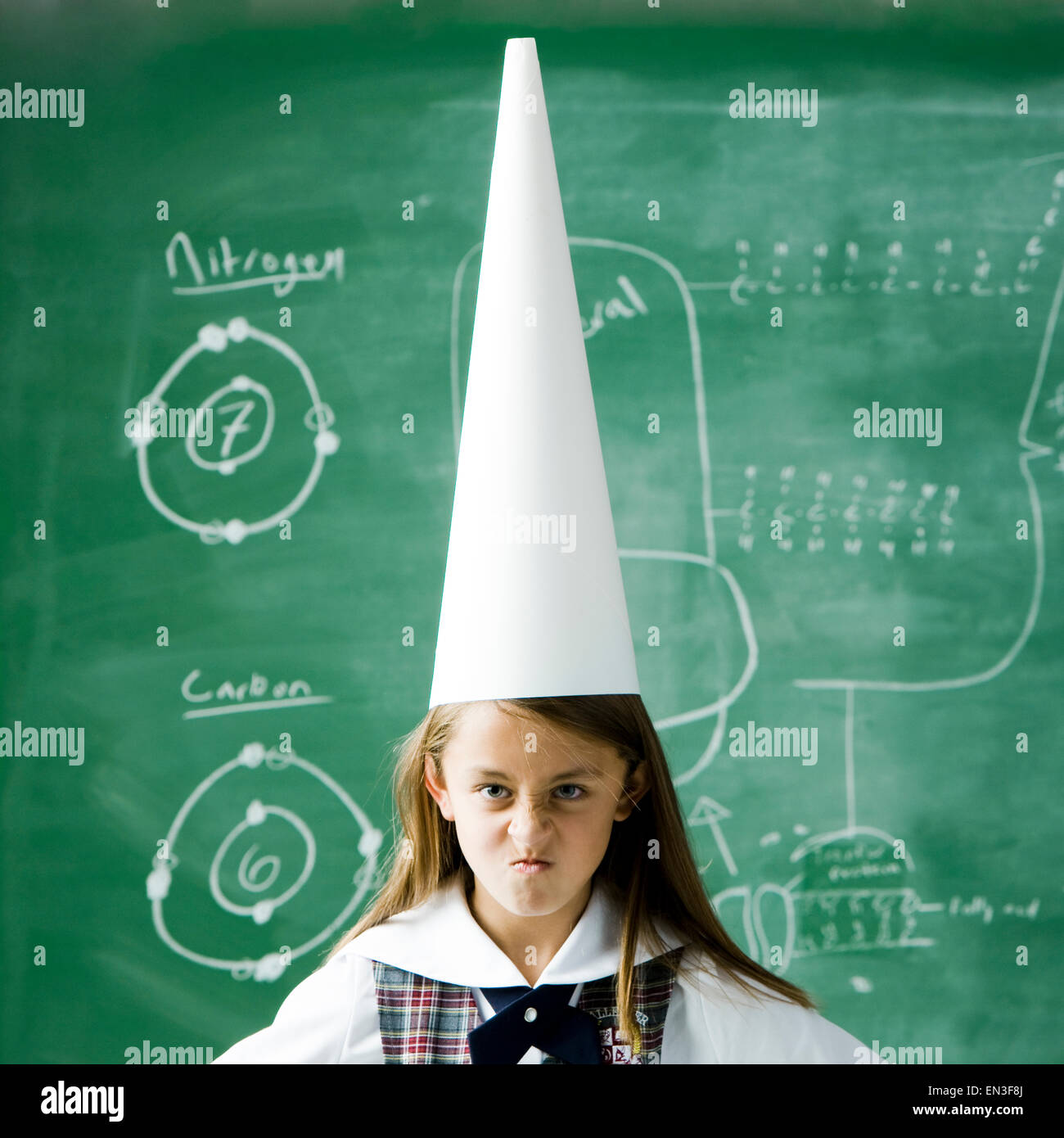 Mädchen im Klassenzimmer stehen vor einer Tafel mit einem Dunce Mütze Stockfoto
