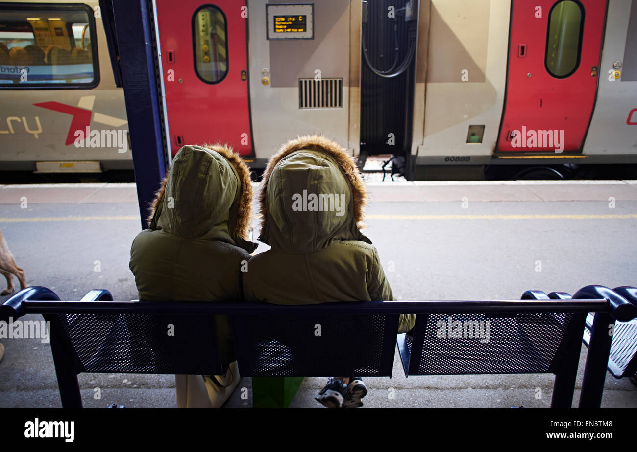 Eineiige Zwillingsmädchen im gleichen Parker Mantel Zug am Bahnhof Oxford warten. Stockfoto
