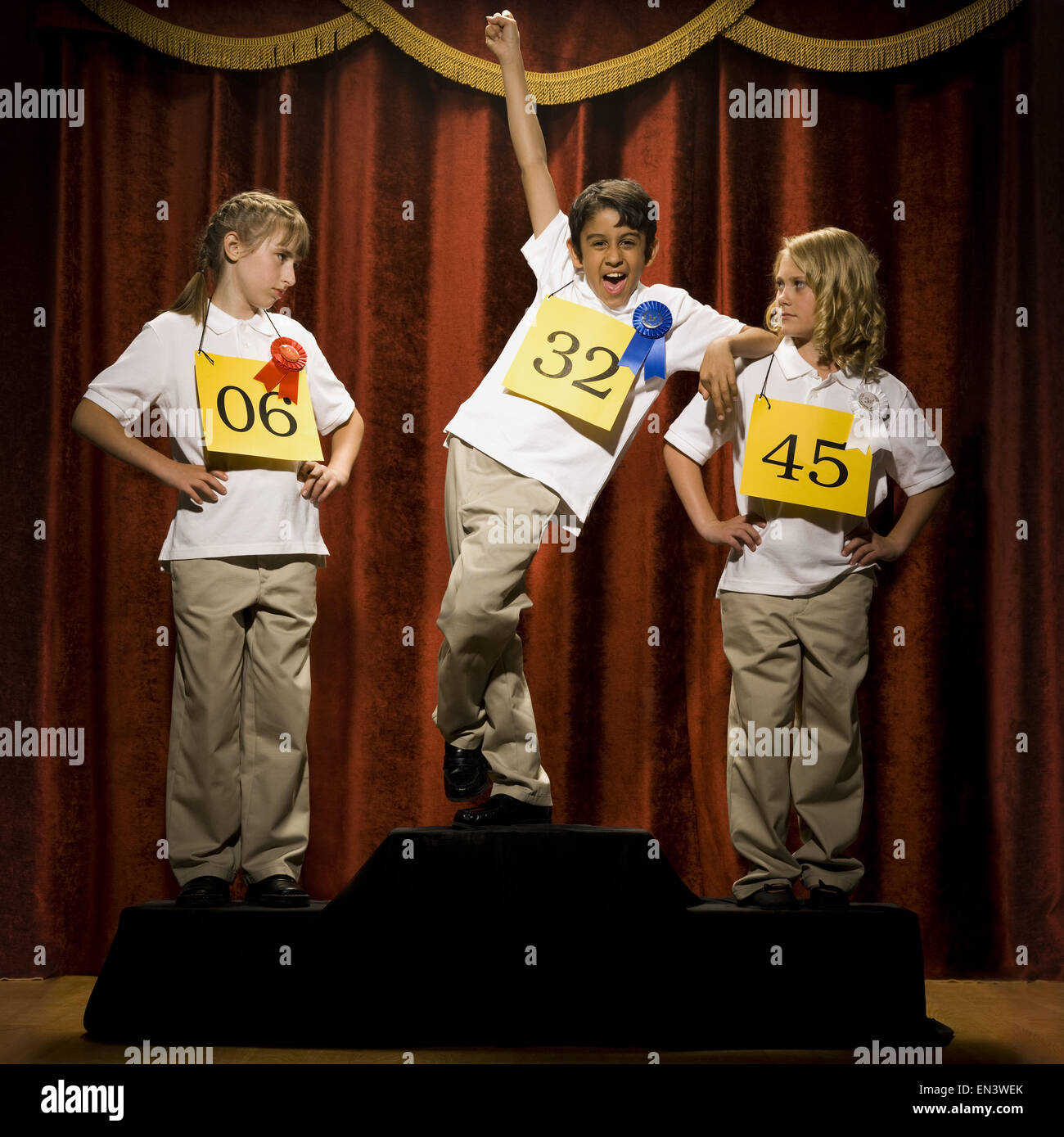 Drei Kinder auf der Bühne am Siegertreppchen mit Bändern lächelnd Stockfoto