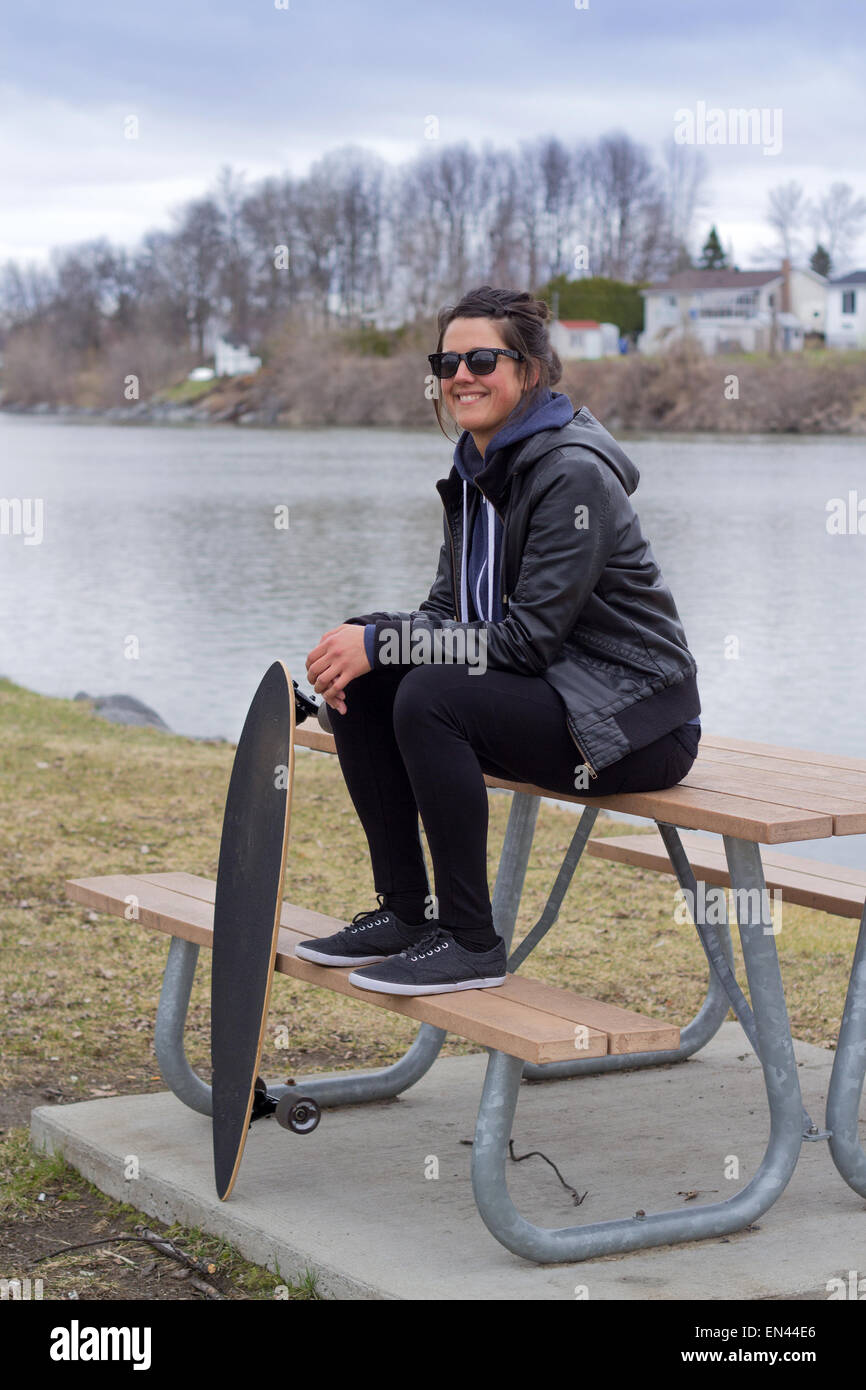 Frau sitzt auf Picknick-Tisch in einem Park mit Longboard zu beruhigen Stockfoto